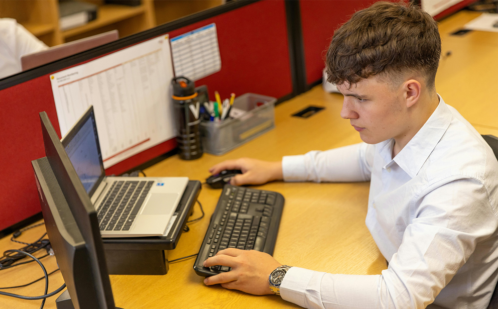 Man seated at a desk in an office cubicle looking at computer screens